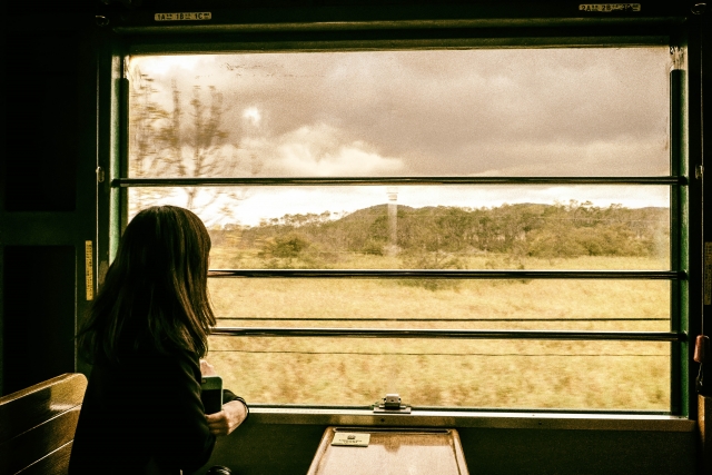 荒野を走る列車の中から車窓を眺める女性イメージ20180307